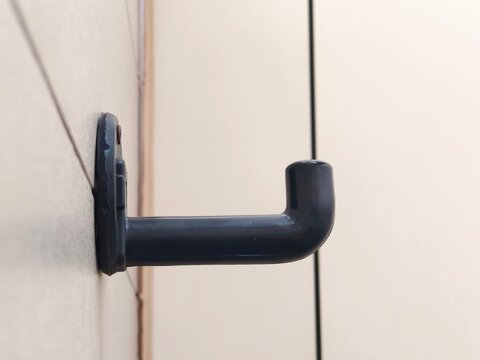 Black hard plastic wall hook mounted on a tiled surface, close-up shot of a minimalist single robe or towel hanger.