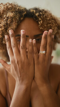Woman smiling with hands framing face, teeth visible, natural curly hair in a bright studio setting; joy confidence.