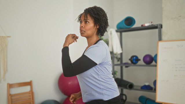 Young woman shadowboxing with clenched fist near exercise mat in a fitness studio; determination focus.