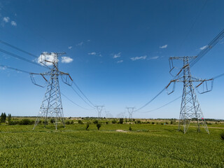 Obraz premium Transmission towers standing in green fields under blue sky