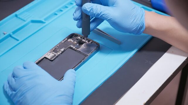technician repairing internal micro-electronics component inside an opened smartphone on a blue mat as a concept for hardware maintenance service, right to repair information technology