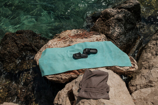 Beach towel, bag, and sandals on seaside rocks