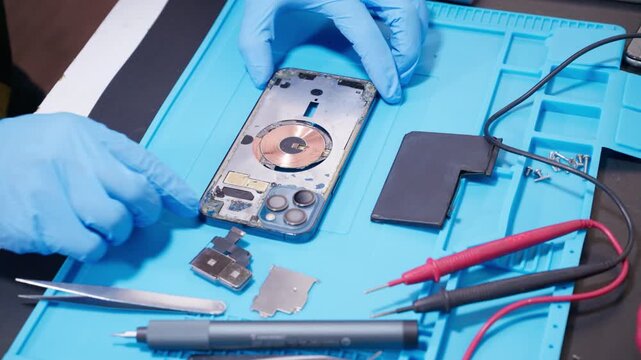 technician repairing internal micro-electronics component inside an opened smartphone on a blue mat as a concept for hardware maintenance service, right to repair information technology