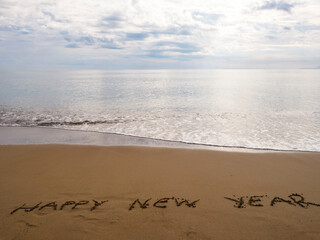 Fototapeta premium Happy New Year message written in beach sand with ocean view