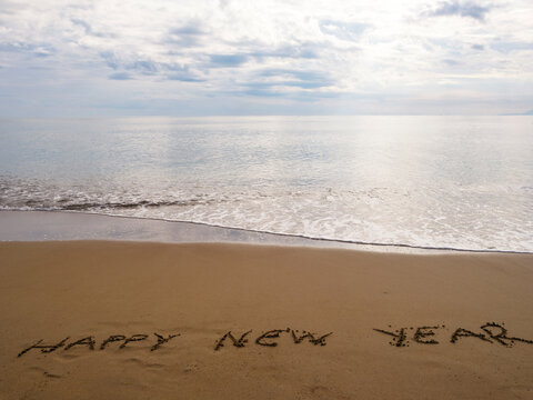 Happy New Year message written in beach sand with ocean view