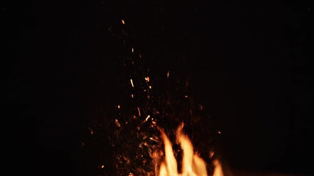 Ember sparks rise from a small bonfire during a dark night with dramatic lighting effects
