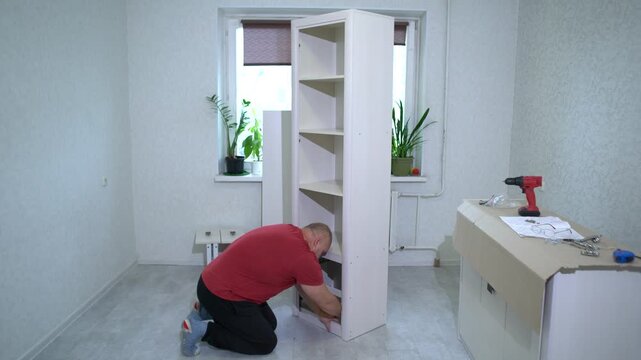A man carefully assembles a modern bookshelf in a bright living room filled with houseplants. The process involves using tools and following instructions to create a functional piece of furniture.