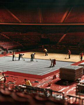 Workers clean a vast arena floor beneath dim red lights