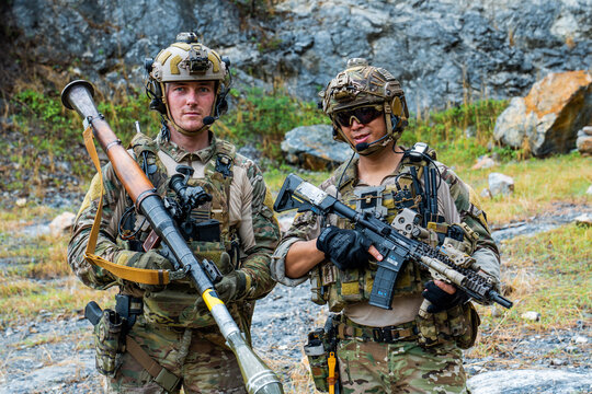Soldiers stand together in tactical gear while holding weapons in a rugged outdoor setting