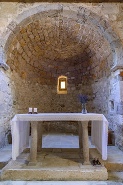 Stone altar with white cloth, lavender and candles in the small apse of an old Romanesque church, warm light from one window