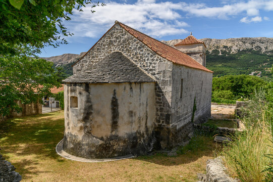 Old Romanesque stone church with a rounded apse under a slab roof and a small bell tower on a Mediterranean island