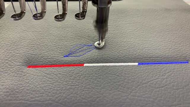 Industrial embroidery machine stitching above on textured synthetic leather material.