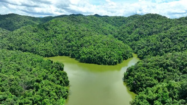 Drone view reveals a peaceful reservoir winding through dense tropical forest, representing water security, natural ecosystems, biodiversity and environmental conservation. Phrae Province, Thailand.
