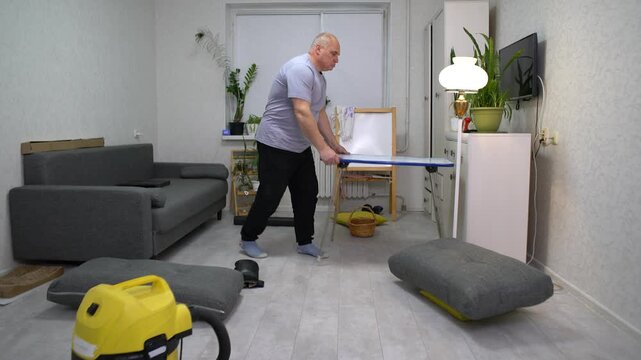 Man tidies up a living room by arranging furniture, using a vacuum cleaner, and decluttering surfaces to create a more organized space for spring cleaning.