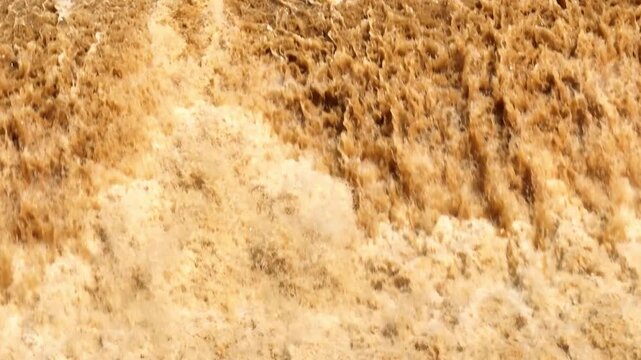 Drone perspective reveals fierce brown floodwater and foaming currents, conveying severe rainfall, climate extremes, natural hazards, water erosion and increasing flood risk. Phrae Province, Thailand.
