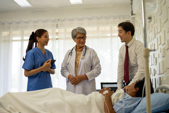 Hospital nurse with tablet talking to doctor at patient bedside
