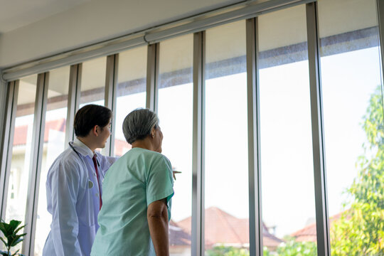Doctor talking with senior woman by bright window from behind