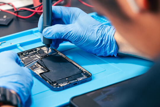 technician repairing internal micro-electronics component inside an opened smartphone on a blue mat as a concept for hardware maintenance service, right to repair information technology