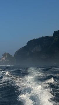 A scenic view of a misty coastline with rocky cliffs and waves in the foreground. The sky is clear and blue, creating a serene atmosphere.