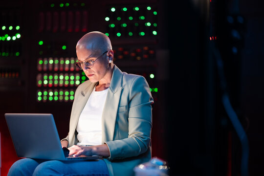 Bald woman programmer working on laptop in server room