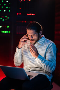 Man talking on phone using laptop in server room