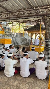 A group of young Asian men in white traditional attire sit in prayer at a temple. They are focused and respectful, surrounded by a serene environment.