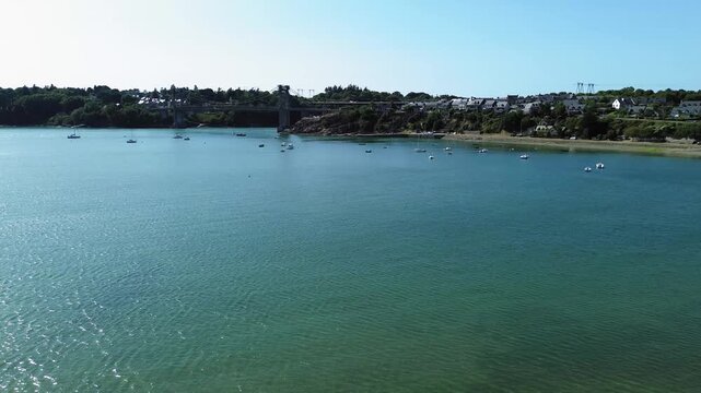 Aerial drone view of the Rance estuary near Saint-Jean in Brittany, France, with Pont Saint-Hubert visible in the background. Numerous sailboats are anchored in the calm blue-green waters, surrounded