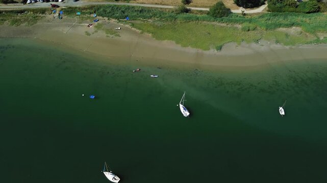Aerial drone view of the Rance estuary near Saint-Jean in Brittany, France, showing small sailing boats anchored along the muddy tidal shoreline and a peaceful coastal landscape.