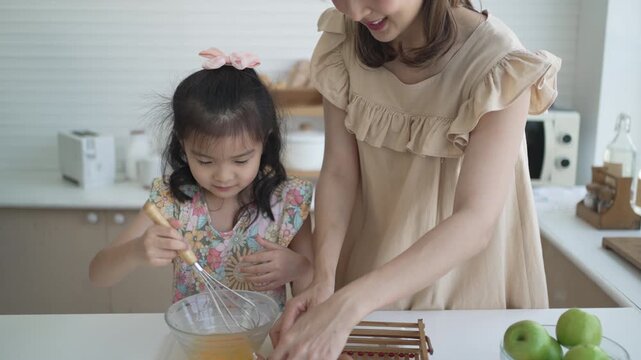 Mother watching daughter whisk egg mixture in kitchen bowl
