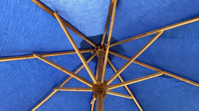 Low angle view of blue beach umbrella with wooden frame
