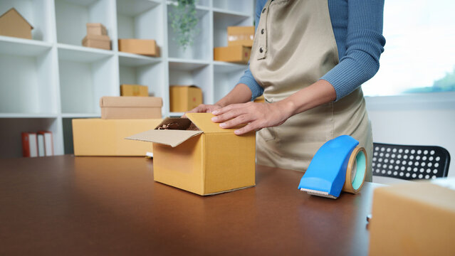 Small business owner taping cardboard box for online store order shipping and delivery