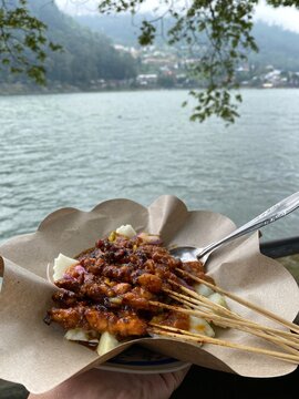 Delicious Indonesian Chicken Satay Served on Brown Paper with Scenic Lake View Background