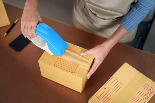 Cropped hands taping cardboard box for small business online order fulfillment