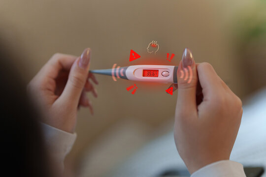 Cropped hands holding digital thermometer showing high fever reading for health diagnosis
