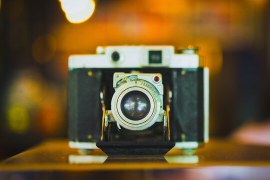 Vintage photography and retro camera concept, antique folding bellows camera with chrome lens resting on table with warm bokeh, symbolizing analog technology, photojournalism, and hobby.