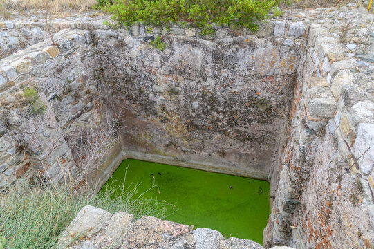 Ancient stone-walled cistern filled with bright green algae water seen from above at the Lekythos fortress, Toroni, Sithonia, Chalkidiki, Greece