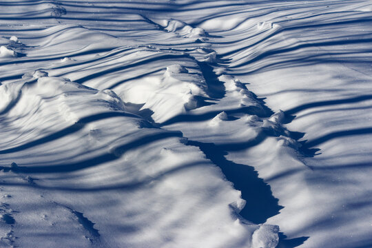 Sparkling white snowdrifts in a sunlit field, featuring rhythmic long blue shadows and crisp textures on a bright frosty winter day with serene natural patterns across the terrain