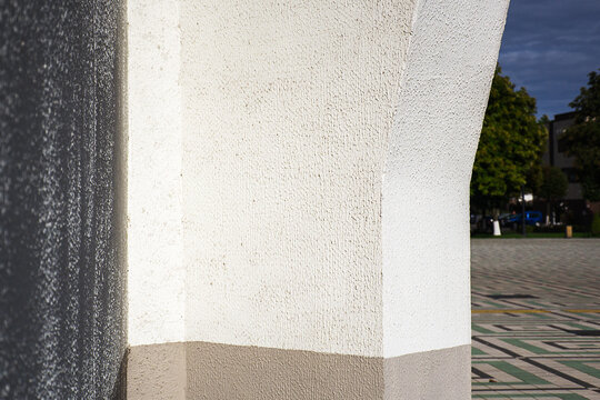 Close up of white textured plaster column with gray base casting shadow on sunny day outdoors with copy space