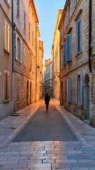 Fototapeta premium Narrow old town street at dawn with person walking away