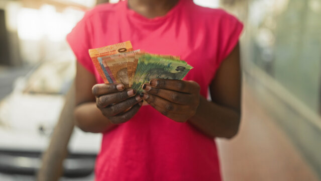 Woman holds fanned rand banknotes in hands on street with parked car and shopfronts; financial confidence.