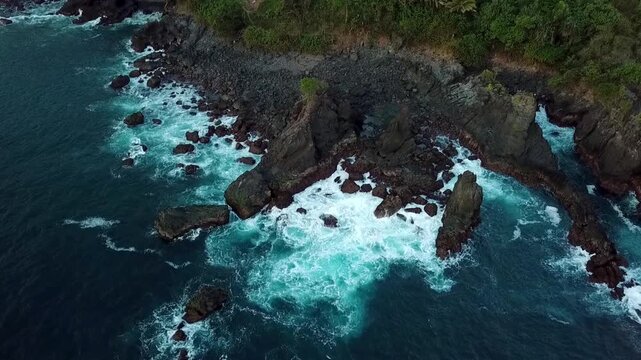 Top-down aerial drone footage of ocean waves crashing against rocky cliffs at Rajaan Beach in Trenggalek, East Java, Indonesia.