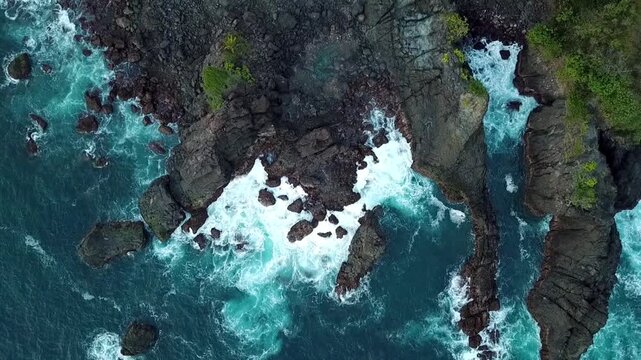 Top-down aerial drone footage of ocean waves crashing against rocky cliffs at Rajaan Beach in Trenggalek, East Java, Indonesia.