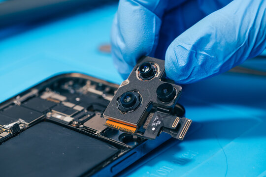 technician repairing internal micro-electronics component inside an opened smartphone on a blue mat as a concept for hardware maintenance service, right to repair information technology