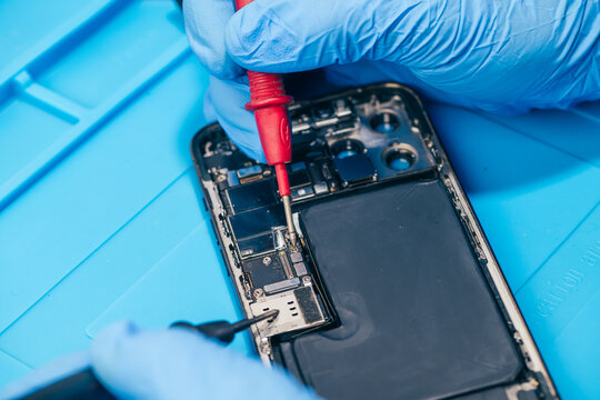 technician repairing internal micro-electronics component inside an opened smartphone on a blue mat as a concept for hardware maintenance service, right to repair information technology