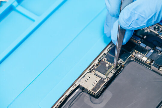 technician repairing internal micro-electronics component inside an opened smartphone on a blue mat as a concept for hardware maintenance service, right to repair information technology