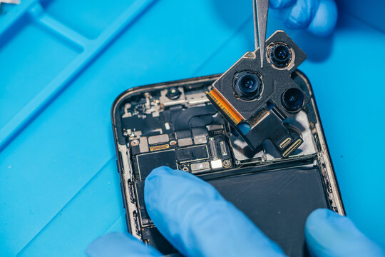 technician repairing internal micro-electronics component inside an opened smartphone on a blue mat as a concept for hardware maintenance service, right to repair information technology
