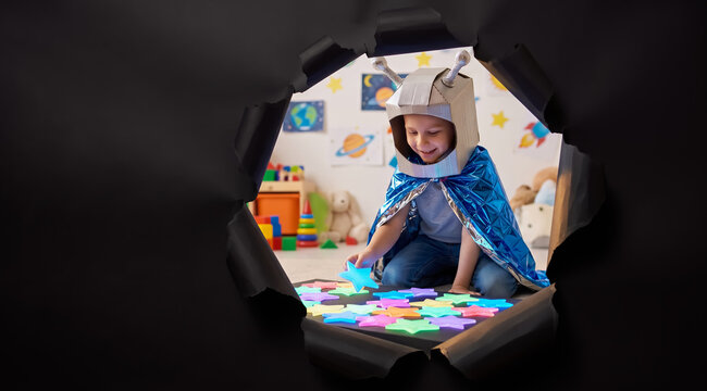 Young child wearing homemade alien costume playing with colorful star shaped toys on floor, view through torn black paper. Childhood, imagination, creative play, pretend roleplay.