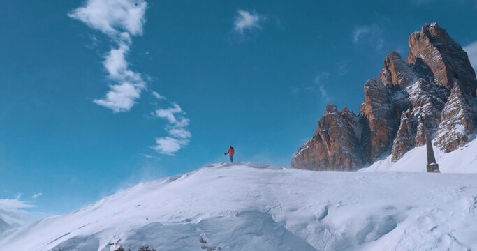 Ski mountaineer crossing a snowy ridge in the Dolomites with dramatic alpine peaks and blue sky in the background, capturing winter adventure and breathtaking mountain landscape.