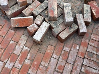 A pile of salvaged clay bricks lying on top of a newly laid herringbone pattern brick patio. © Roger