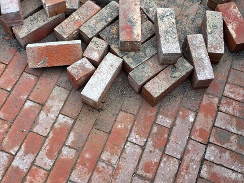 A pile of salvaged clay bricks lying on top of a newly laid herringbone pattern brick patio.